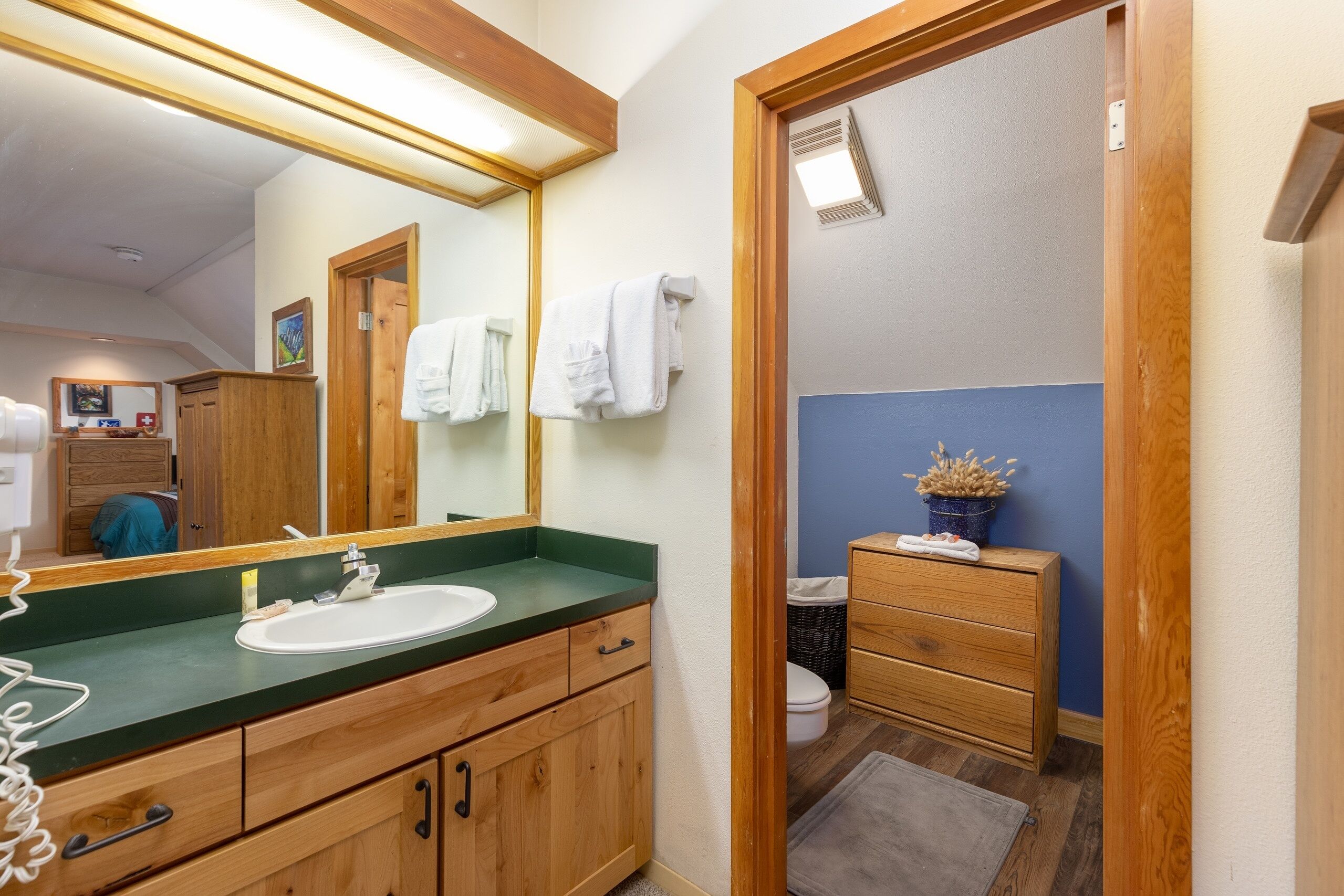 A bathroom with a wooden vanity, a sink, a mirror, and a toilet.