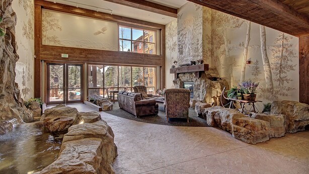 A spacious interior with a stone fireplace, comfortable seating, and large windows offering views of the outdoors. - 8824 The Springs 2 Bedroom Condo by RedAwning (Keystone)