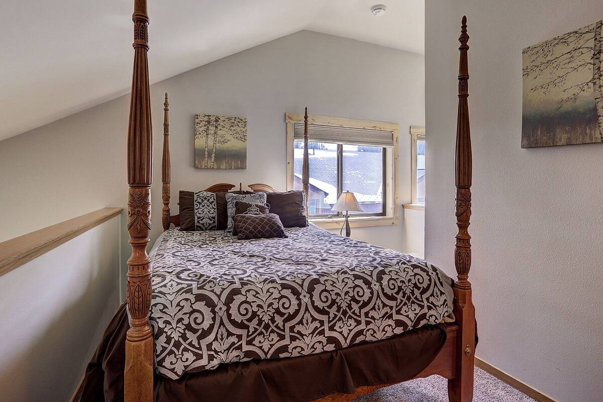 A four-poster bed with a patterned bedspread, a window with a view of a snowy landscape, and a painting on the wall.