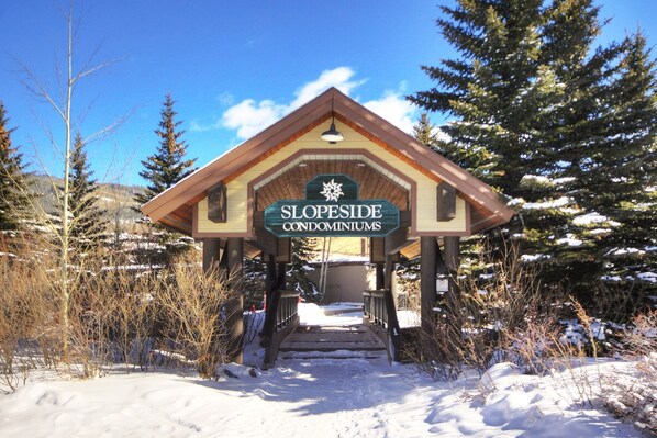 A wooden building with a sign reading "SLOPESIDE CONDOMINIUMS" at the entrance. - 2759 Slopeside 1 Bedroom Condo by RedAwning (Keystone)