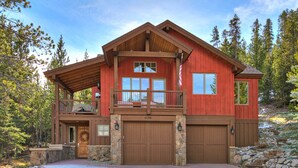 A two-story log cabin with a stone foundation, large wooden garage doors, and a balcony. - 170 Elk Circle by RedAwning (Keystone)