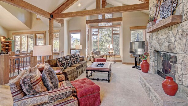 A spacious living room with high ceilings, exposed wooden beams, and large windows offering views of the outdoors. - 170 Elk Circle by RedAwning (Keystone)