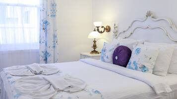 Un letto rifatto con lenzuola a motivi floreali, una lampada da comodino e un quadro appeso al muro.