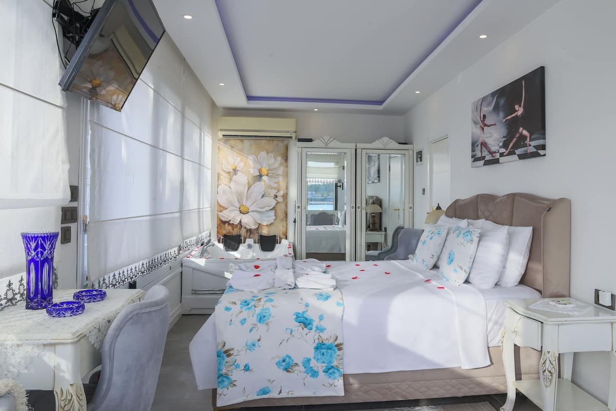 Ein modernes Hotelzimmer mit einem großen Bett, einem Schminktisch mit Spiegel, einer Sitzecke inklusive Tisch und Stühlen sowie einem großen Fenster mit Vorhängen.