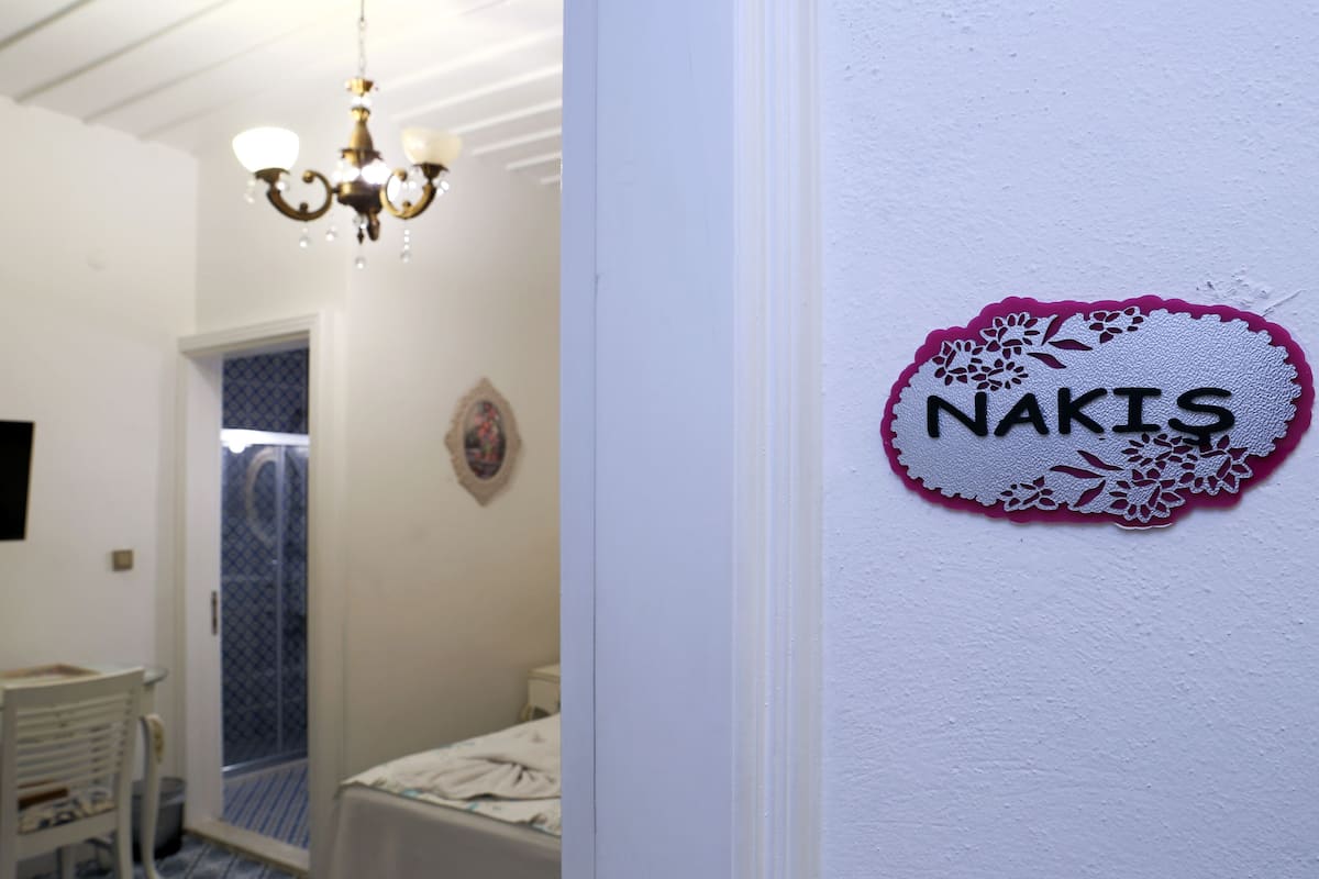 Ein Schlafzimmer mit einem Bett, einer Chandelieber und einem Wandschild mit der Aufschrift 'NAKIS'.
