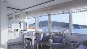 A modern kitchen with white cabinets and a dining area with grey chairs and a white table. - Dantela Butik Hotel (Cesme)