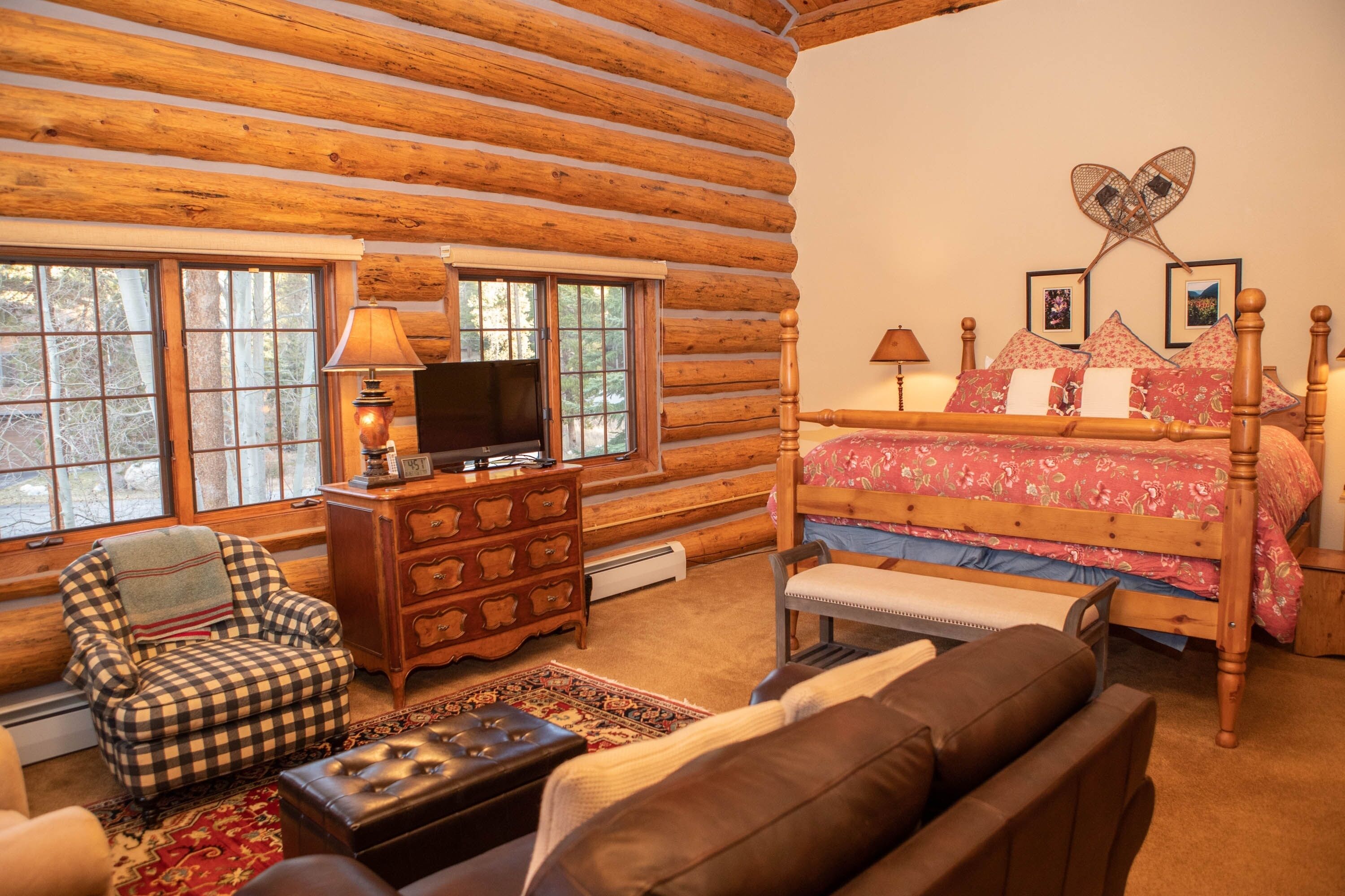 Une chambre dans une cabane en rondins, avec un lit, une commode, une chaise et un téléviseur.