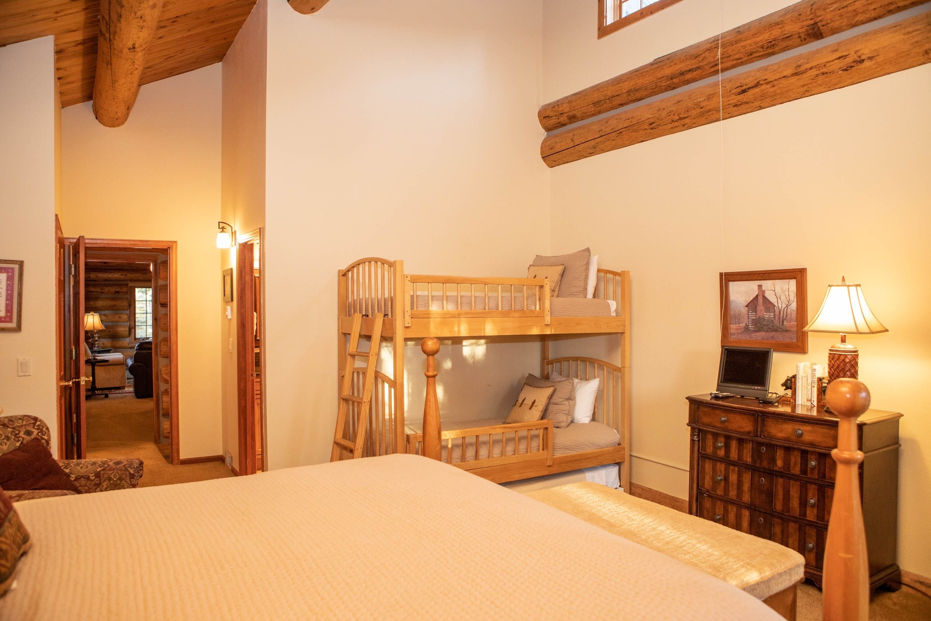 A bedroom with a bunk bed, a desk with a lamp, and a door leading to another room.