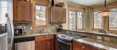 A kitchen with wooden cabinets, a stainless steel dishwasher, a gas stove, and a window overlooking a snowy landscape.