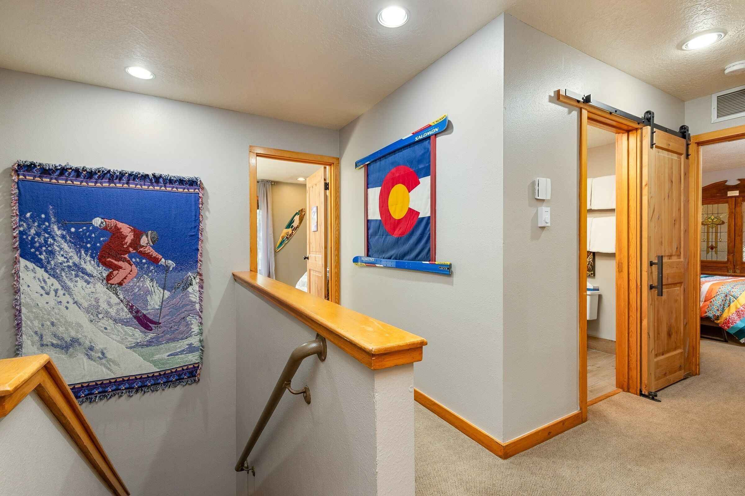 A hallway with a ski-themed tapestry, a Colorado state flag, and a wooden door leading to another room.