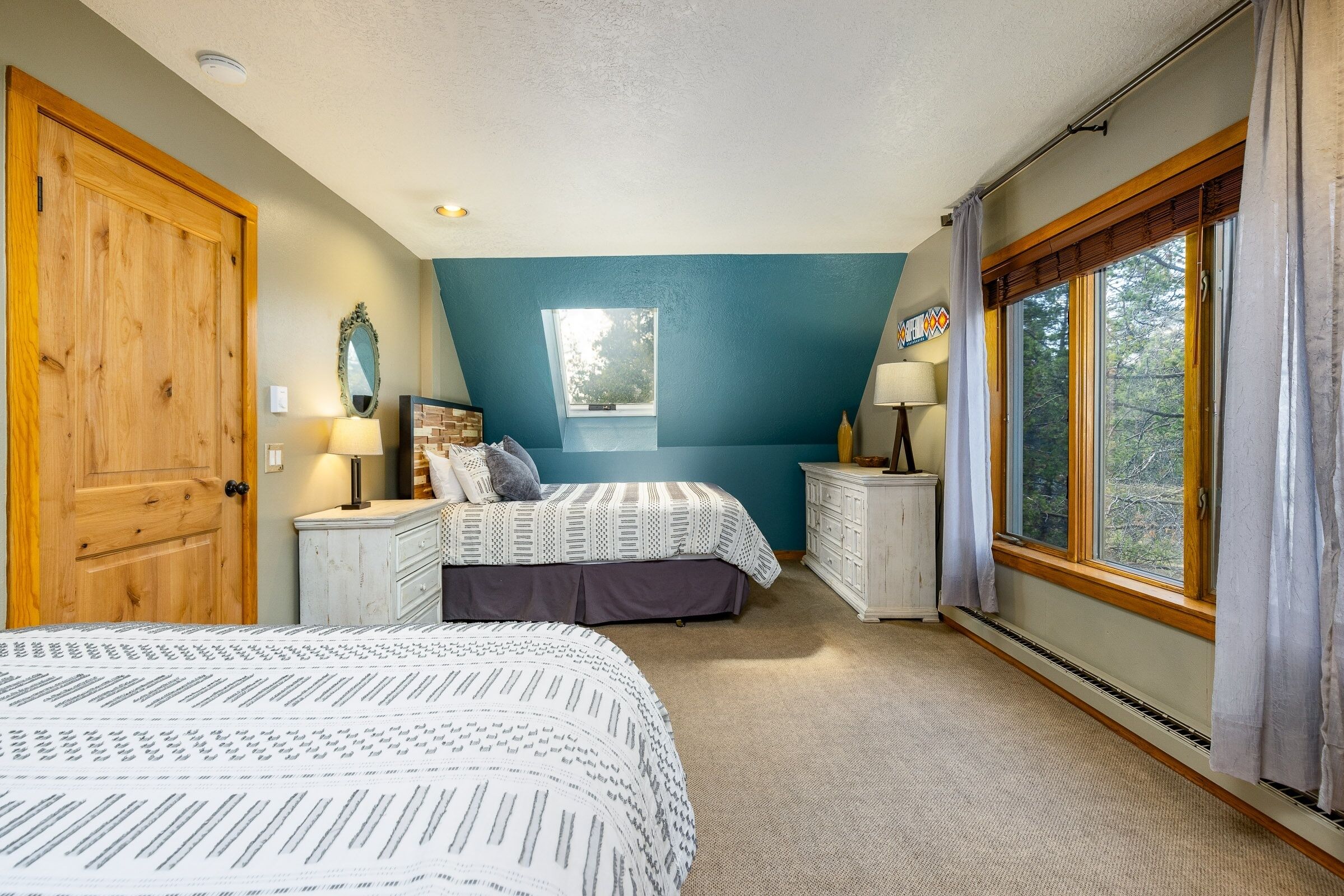 A bedroom with two beds, a large window, and a view of trees.