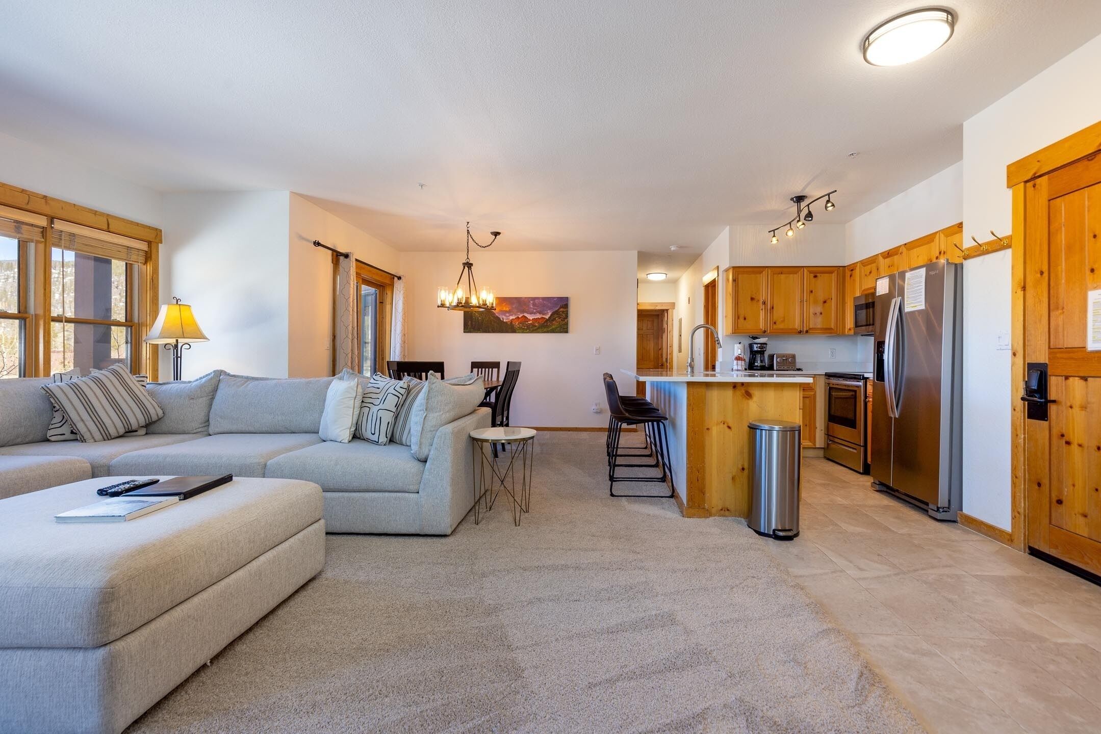 A modern living room with a sofa, a small table, and a kitchen area with wooden cabinets and stainless steel appliances.