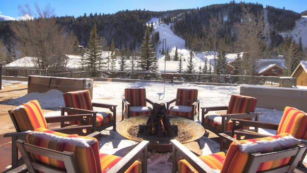 Une terrasse avec des sièges extérieurs et un foyer, offrant une vue sur un paysage montagneux enneigé.