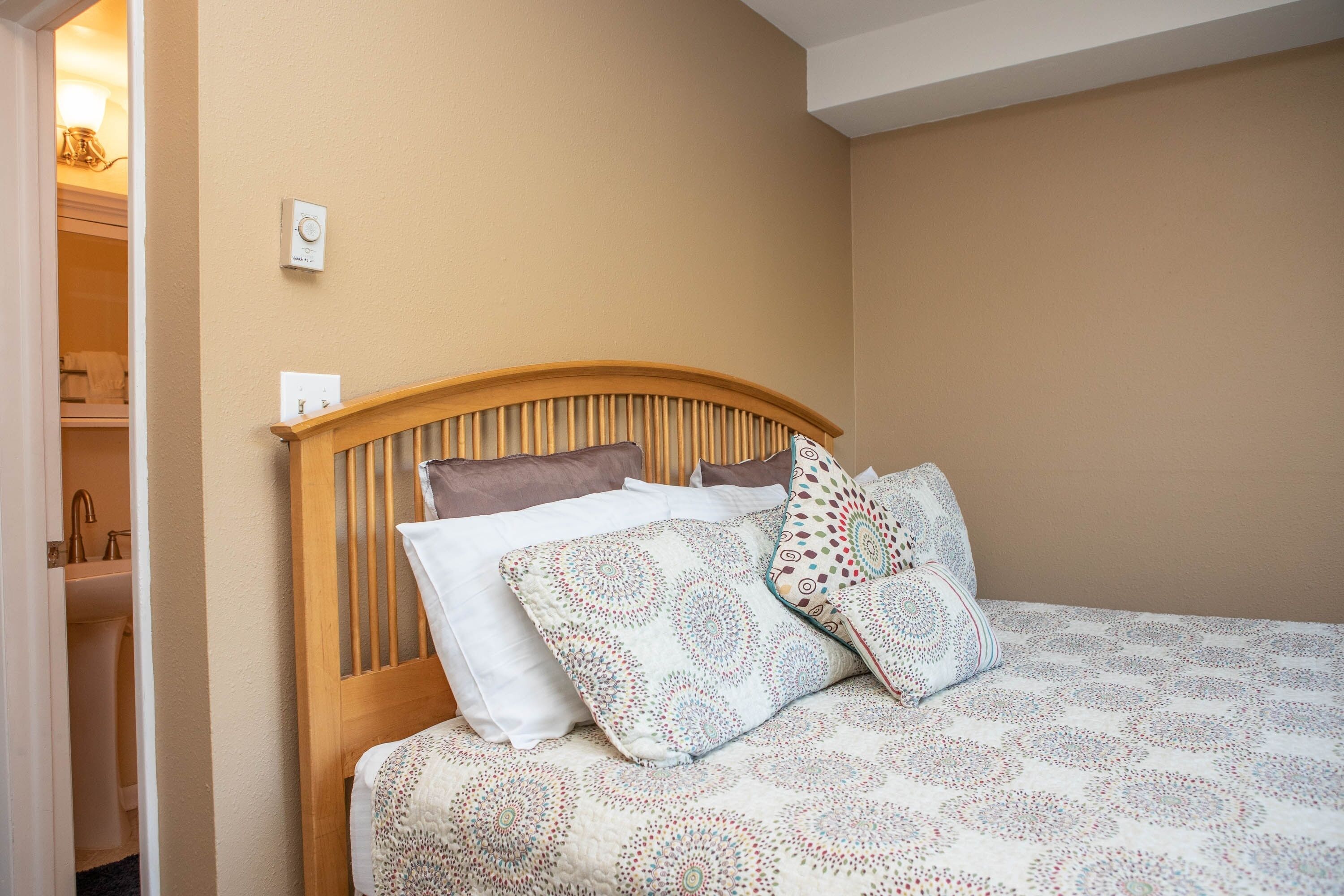 A neatly made bed with a wooden headboard, a white and patterned bedspread, and several pillows.