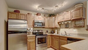 A kitchen with wooden cabinets, stainless steel appliances, a microwave, an oven, a sink, and a clock displaying the time. - 204 Snowdance Manor by RedAwning (Keystone)