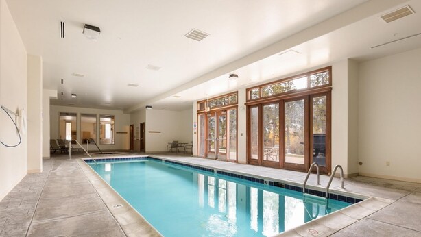 A large indoor swimming pool with clear blue water, surrounded by tiled flooring and large windows.