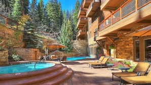 A pool area with a stone wall, lounge chairs, and a wooden building with balconies. - 3056 The Timbers 1 Bedroom Condo by RedAwning (Keystone)