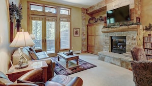 A spacious living room with a stone fireplace, a large flat-screen TV mounted above it, and a cozy seating area with leather sofas and a coffee table. - 3056 The Timbers 1 Bedroom Condo by RedAwning (Keystone)