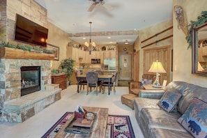 A spacious living area with a stone fireplace, a leather sofa, a dining table with chairs, and a kitchen in the background.