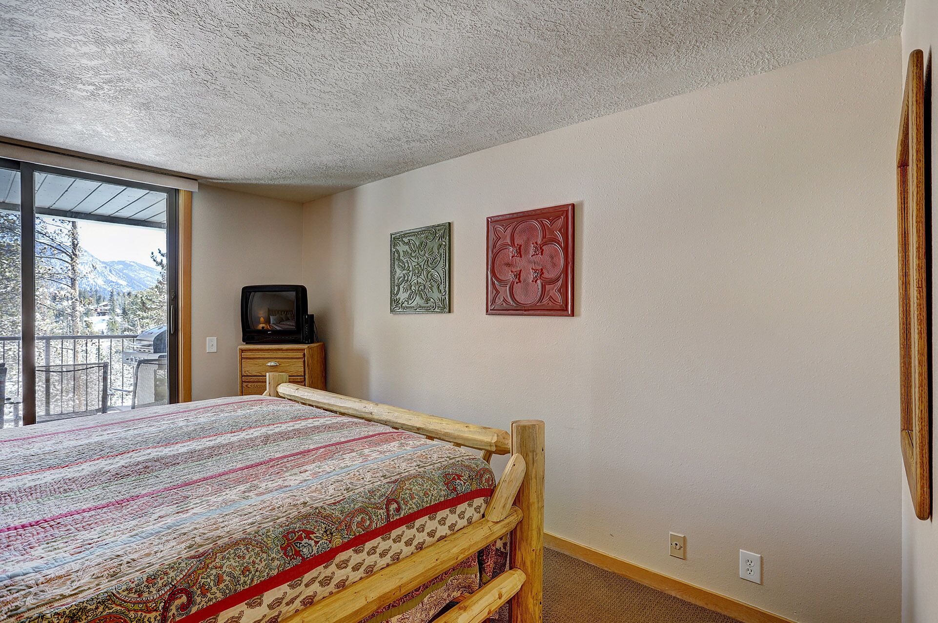 A bedroom with a wooden bed, a television on a wooden cabinet, and two decorative plates on the wall.