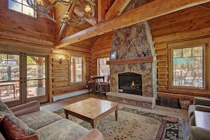 L’intérieur d’une cabane en rondins, avec une cheminée en pierre, des meubles en bois et de grandes fenêtres.