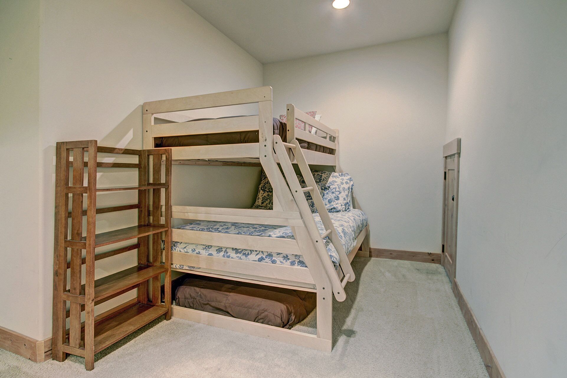 Een stapelbed met een houten ladder en plank, een vloerbedekking en een witte muur.
