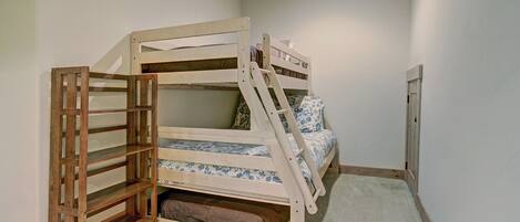 Een stapelbed met een houten ladder en plank, een vloerbedekking en een witte muur.