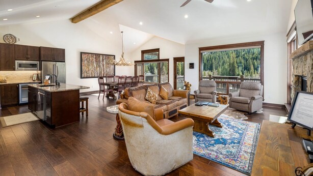 A spacious living area with a large sofa, a coffee table, and a fireplace. There is a kitchen with modern appliances and a dining area with wooden furniture. - 47 River Run Townhomes 3 Bedroom Townhouse by RedAwning (Keystone)