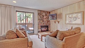 Un salón acogedor con chimenea de piedra, sofás cómodos, un televisor y un ventanal con cortinas.