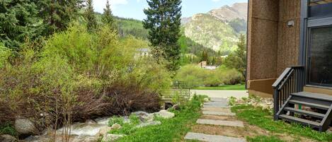 A stone staircase leading to a building with a glass door, surrounded by greenery and a mountain view.
