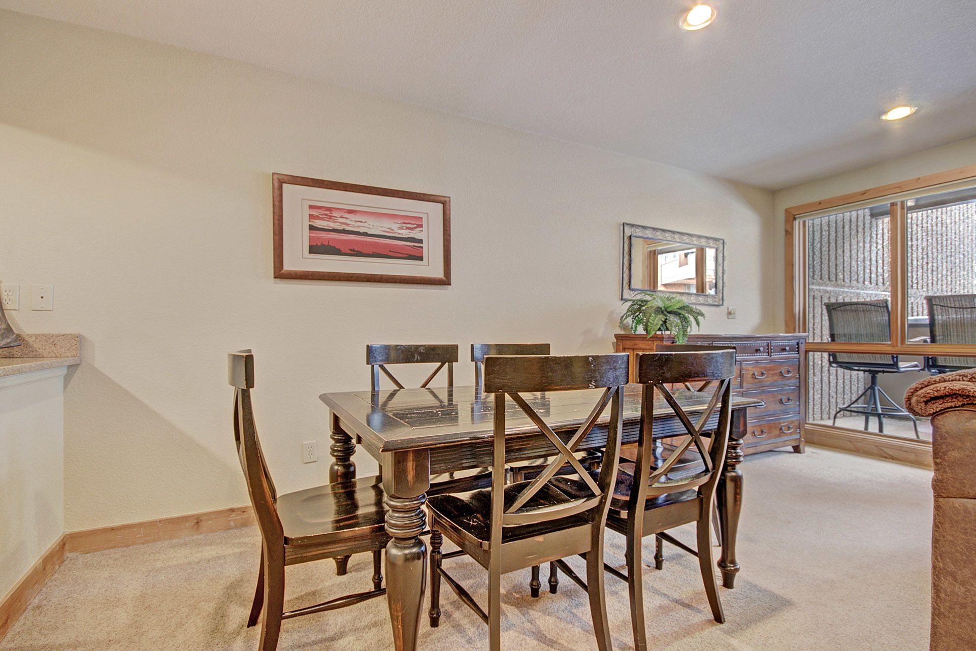 A dining area with a glass-top table, wooden chairs, and a framed picture on the wall.