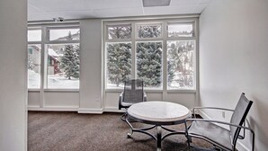 A conference room with a round table and two chairs, large windows with a view of snow-covered trees and a building.