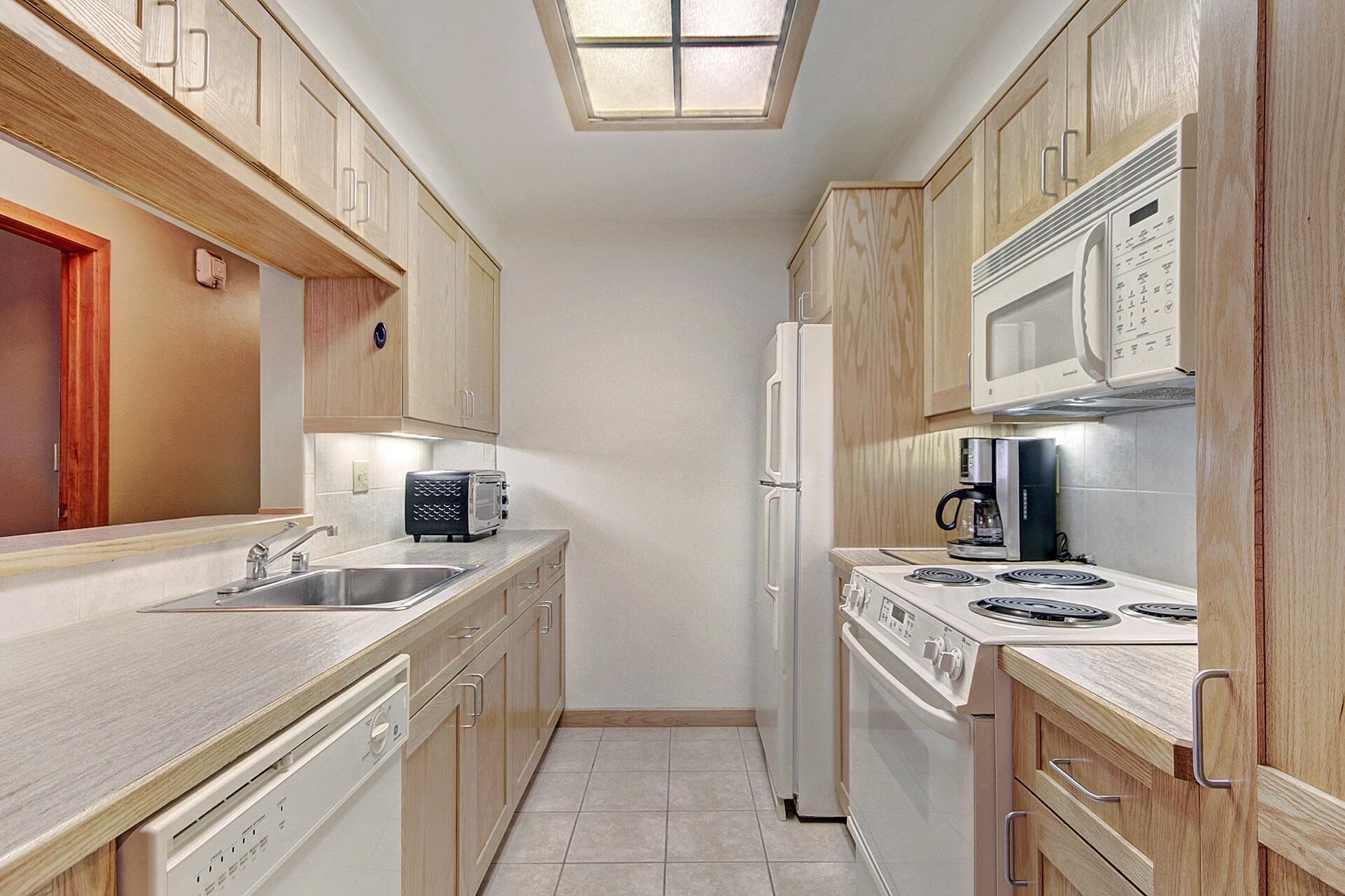 Una cocina estrecha con armarios de madera, un microondas, un refrigerador, una cafetera y un lavavajillas.