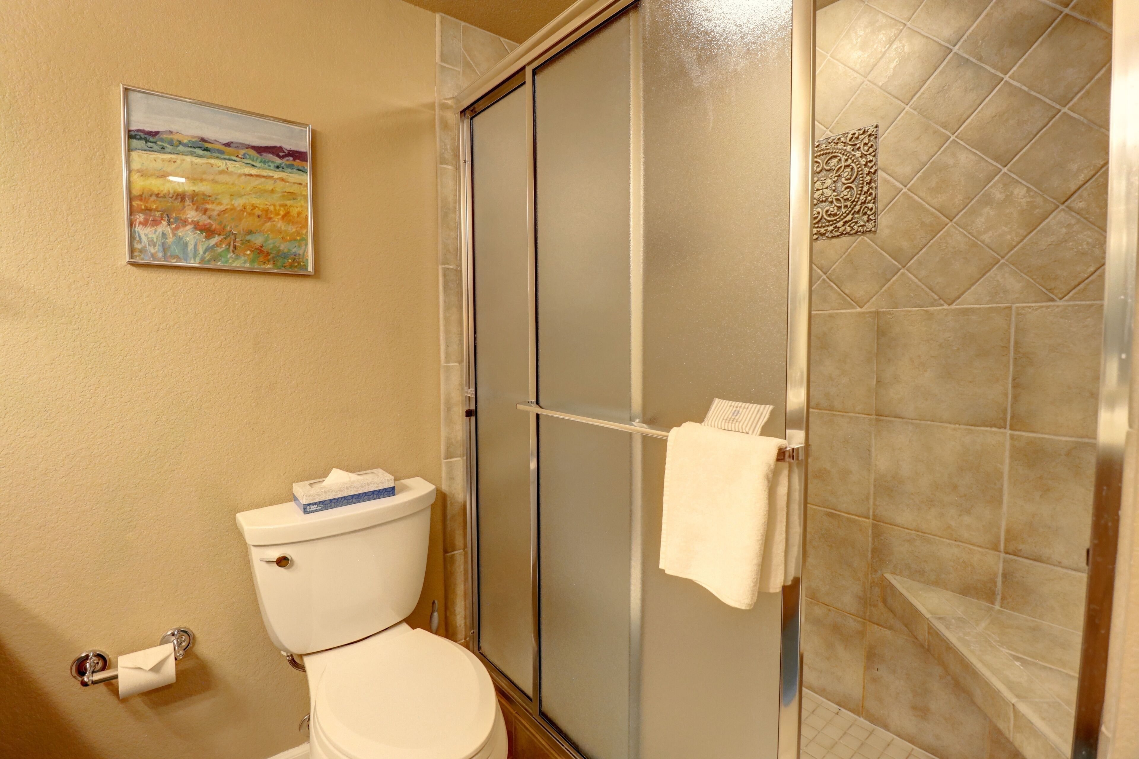 Un bagno con il water, cabina doccia in vetro e un asciugamano appeso alla porta della doccia.