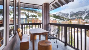 A balcony with a wooden table and chairs, overlooking a mountainous landscape with buildings.