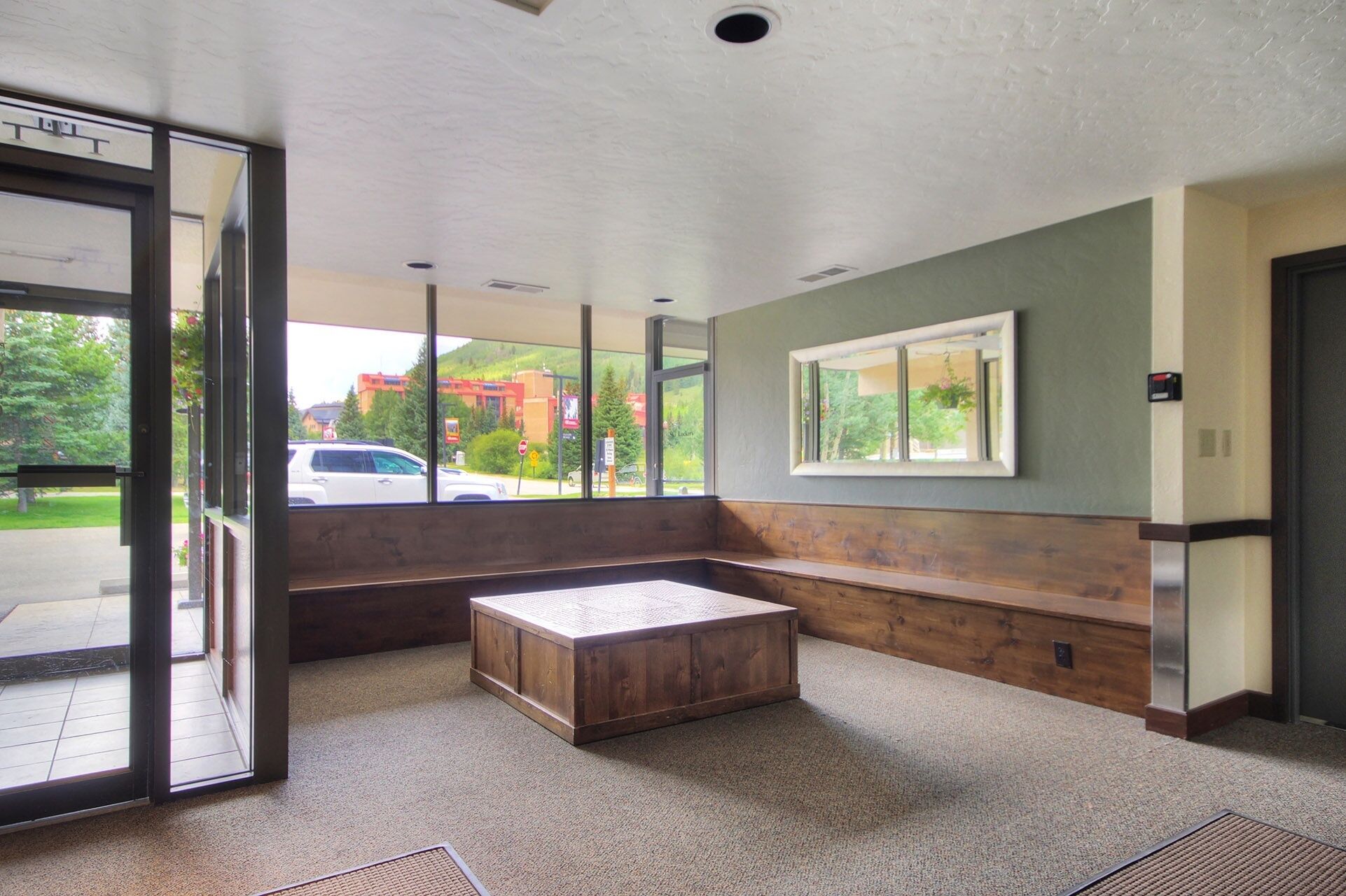 A modern lobby with a bench, a large window, and a door leading outside.
