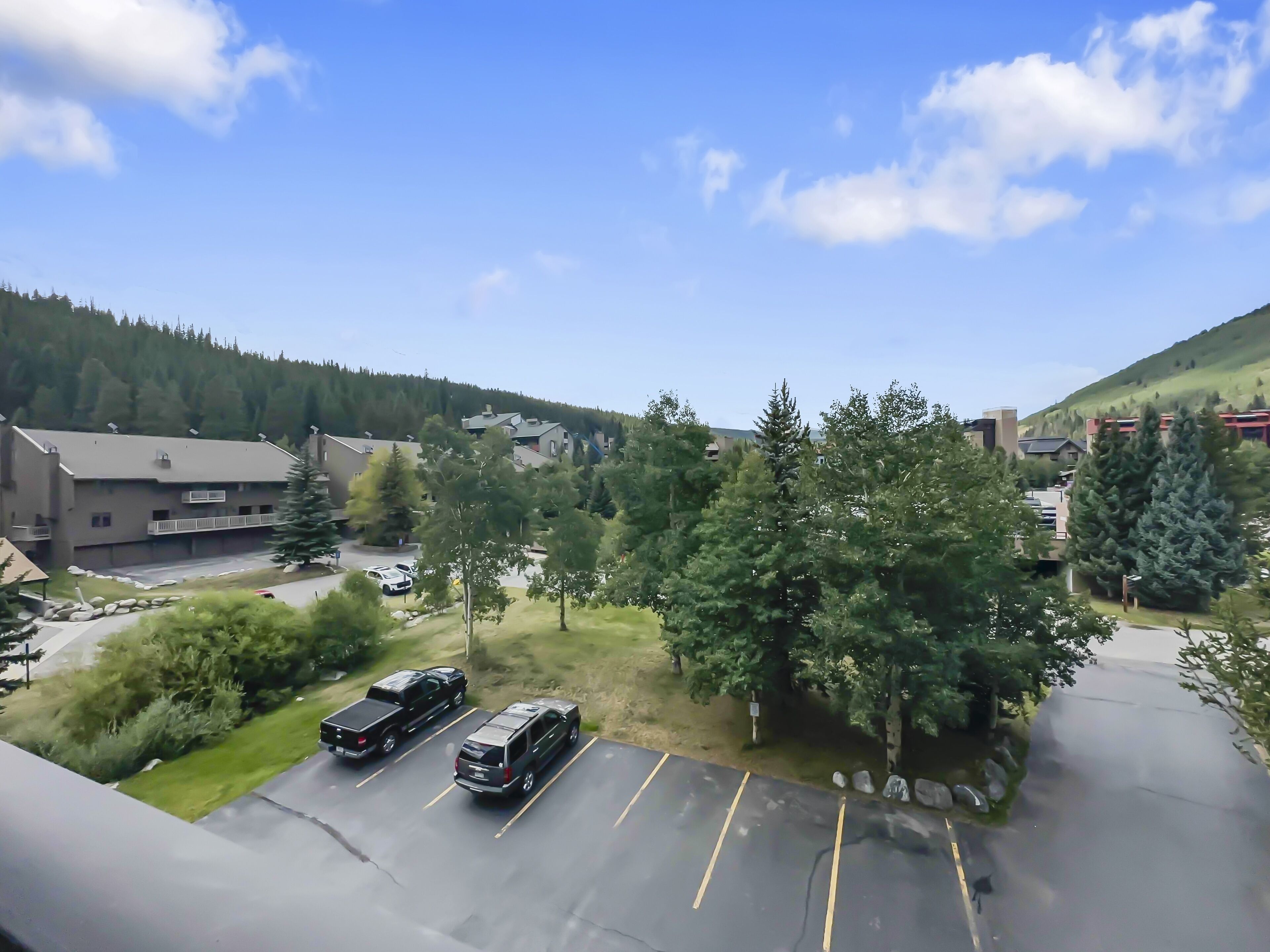 A parking lot with two SUVs, surrounded by trees and buildings.