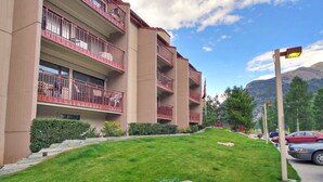 A multi-story hotel with balconies, a well-maintained lawn, and a mountainous backdrop.