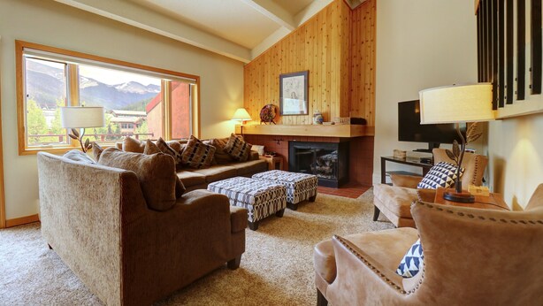 A cozy living room with a fireplace, comfortable seating, and a large window offering a mountain view.