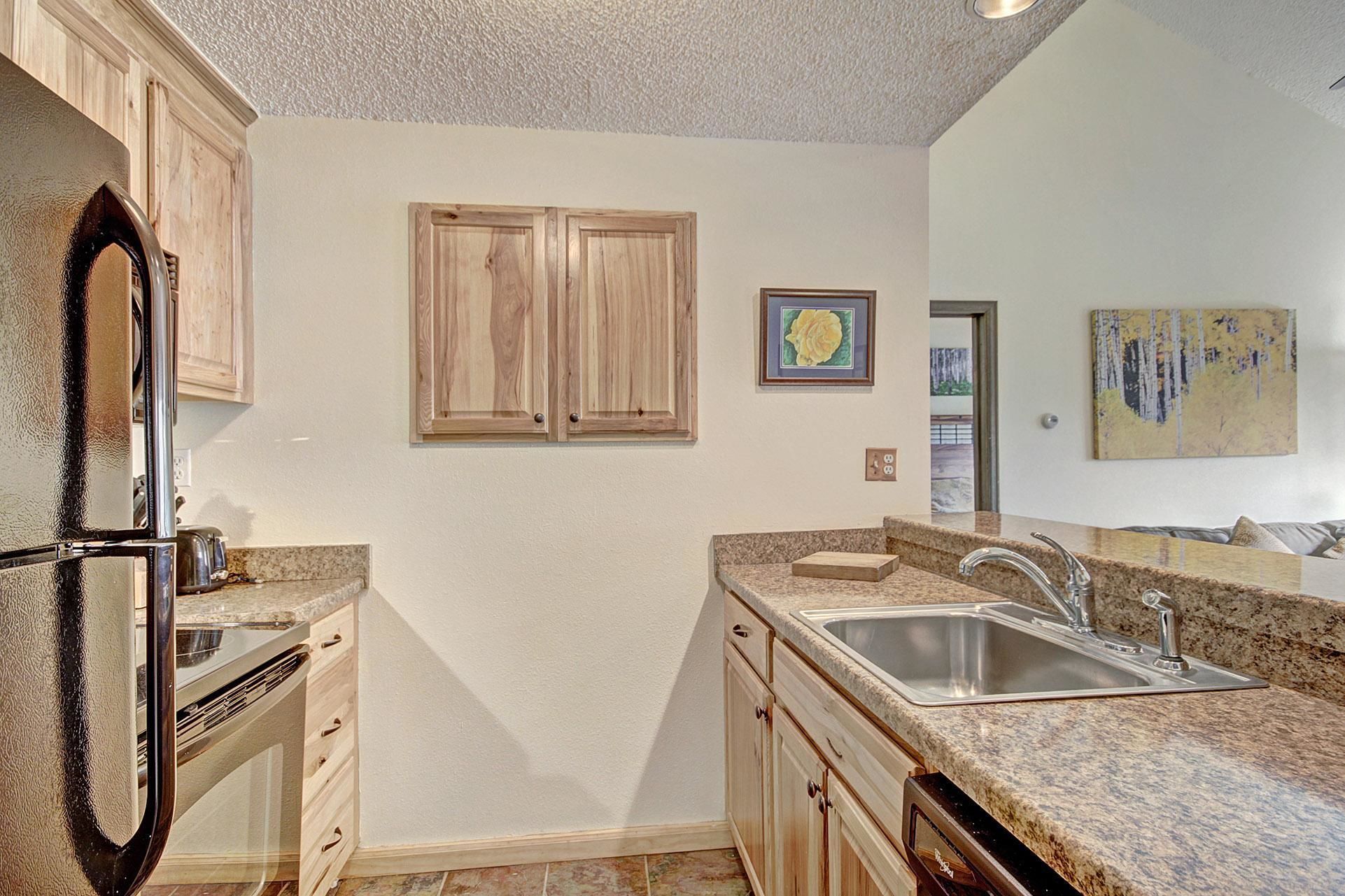 A kitchen with wooden cabinets, a stainless steel sink, granite countertops, and a refrigerator.