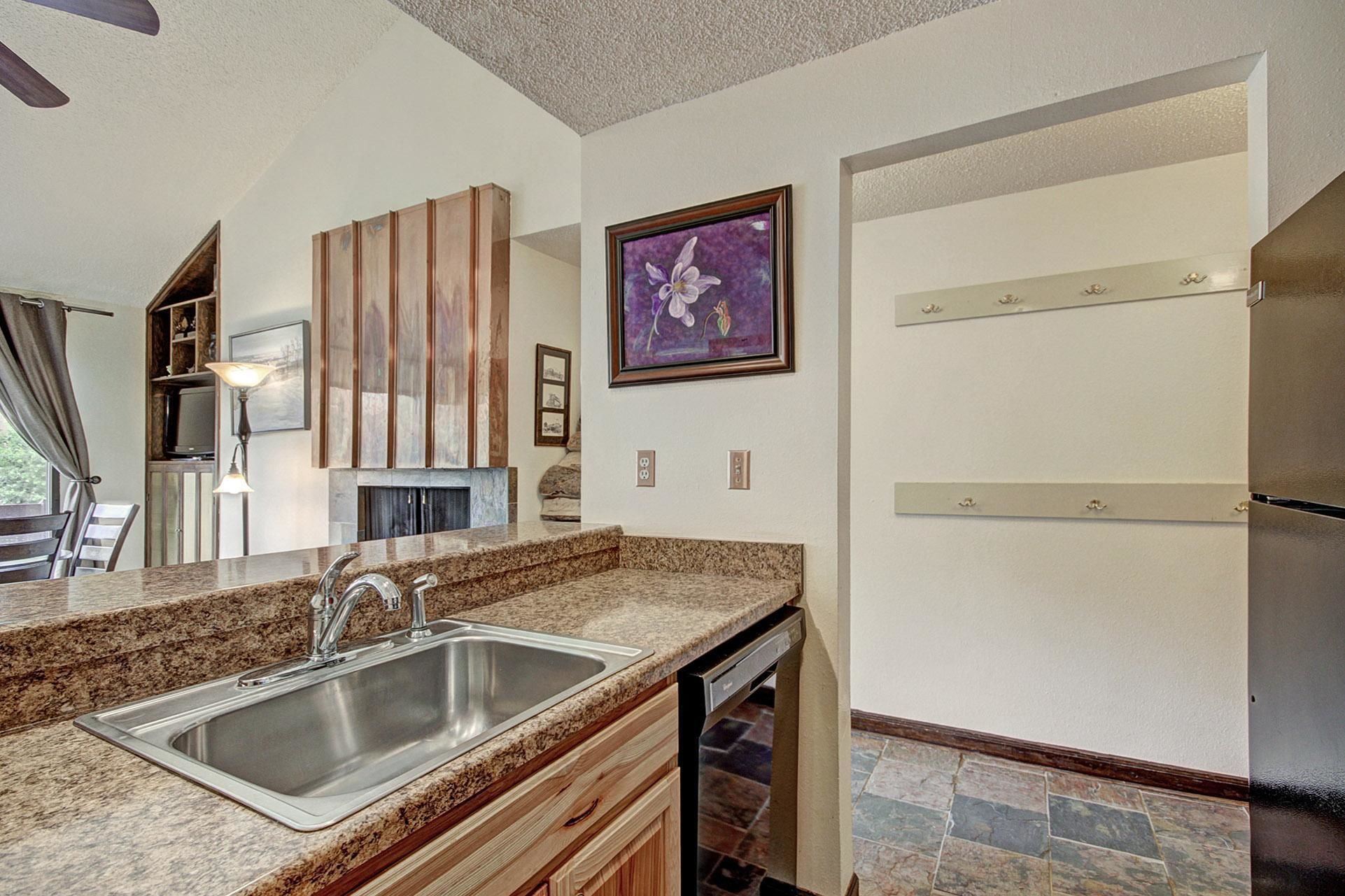 A kitchen with granite countertops, a stainless steel sink, wooden cabinets, a built-in dishwasher, and a refrigerator.