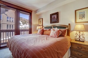 Une chambre avec un grand lit, une tête de lit en bois, deux lampes de chevet et une vue sur un paysage enneigé, visible à travers une porte-fenêtre coulissante.