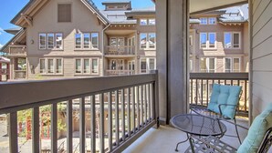 A balcony with a metal table and chairs, overlooking a multi-story building with large windows and a balcony.