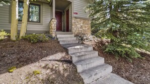 A two-story house with a stone foundation, a red door, and a stone staircase leading to the front door.
