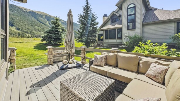 A deck with outdoor furniture, a stone balustrade, and a view of a house with a mountain backdrop.