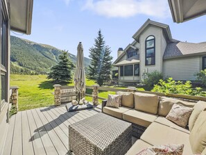 Eine Terrasse mit Gartenmöbeln, einer Steinbrüstung und Blick auf ein Haus mit Bergpanorama.