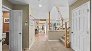 A spacious hallway with carpeted floors, white doors, and a staircase leading to a balcony.