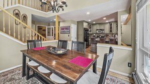 A dining area with a wooden table, chairs, and a chandelier. A staircase leads to an upper level.