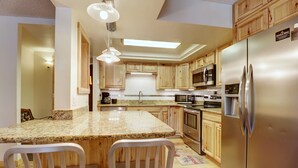 A modern kitchen with wooden cabinets, granite countertops, stainless steel appliances, and pendant lighting.