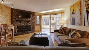 A cozy living room with a stone fireplace, a large flat-screen TV, and a comfortable seating area with a sofa and ottoman.